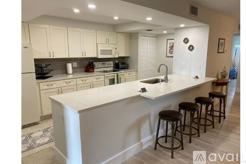 A kitchen with white cabinets and a white island with four black stools.