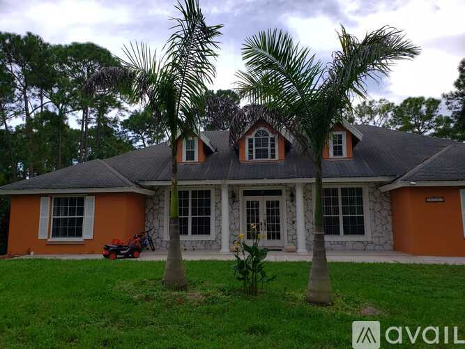 A house with orange walls and a grey roof is surrounded by greenery.