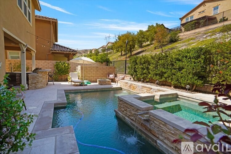 A pool with a waterfall and a hot tub in a backyard.