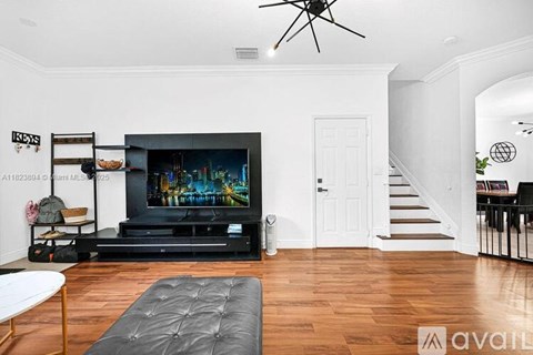 A living room with a television and a black leather ottoman.