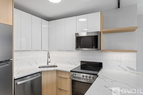 A kitchen with a stainless steel refrigerator, a microwave above the stove, and a marble countertop.