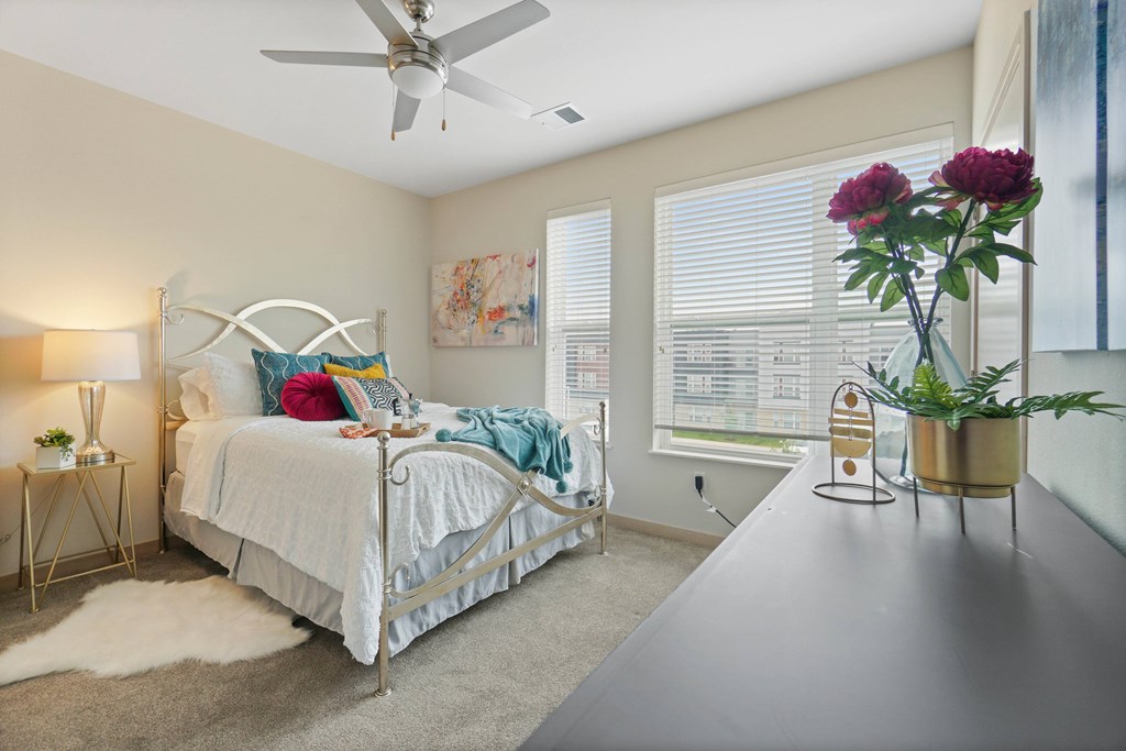 A bedroom with a bed, a fan, and a vase of flowers.
