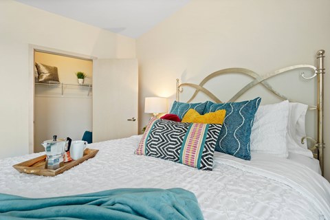 A bed with a white comforter and a tray with cups and a plant on it.