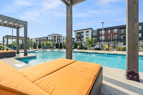 A pool with a sun lounger in the foreground and apartment buildings in the background.
