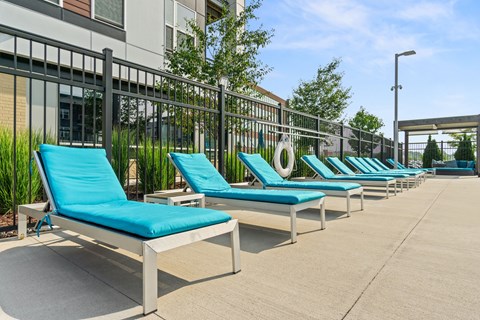 A row of blue sun loungers are lined up on a concrete patio.