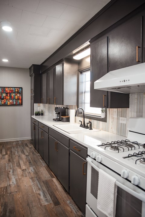 A kitchen with a white stove top oven and dark wood cabinets.