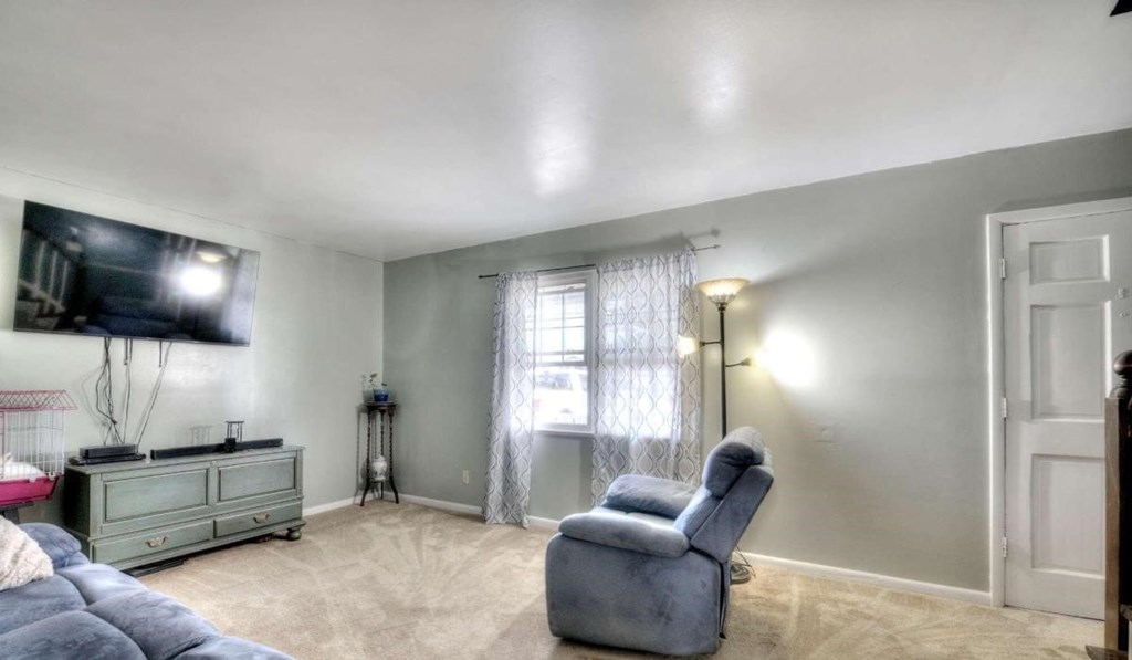 A living room with a grey couch, a grey chair, and a television mounted on the wall.
