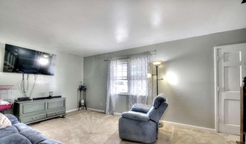 A living room with a grey couch, a grey chair, and a television mounted on the wall.