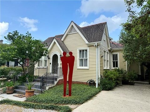 A yellow house with a red sculpture in front.