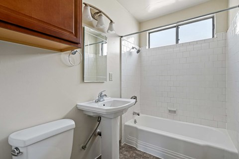 A white sink is on a white pedestal in a white tiled bathroom.