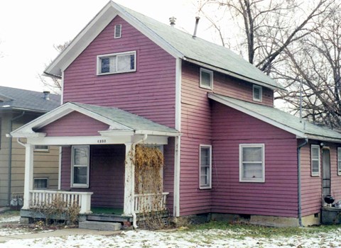 A red house with a white porch and a yellowish snow on the ground.