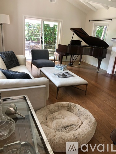 A living room with a white couch, a black chair, a coffee table, a piano, and a glass table with a wine glass on it.