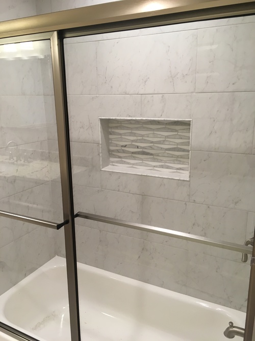 A white bathtub with a glass door and a marble wall.