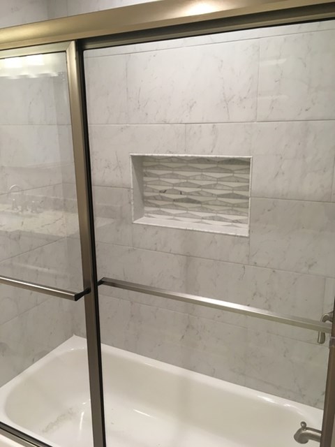 A white bathtub with a glass door and a marble wall.