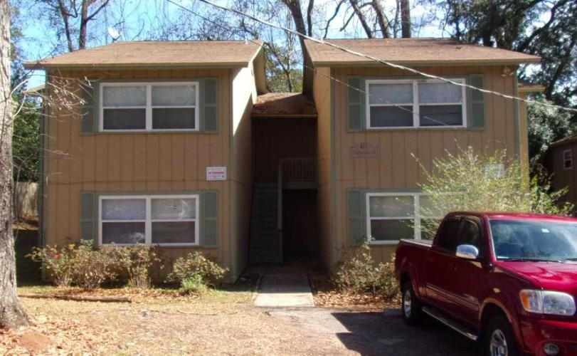 A red truck is parked in front of a tan house.