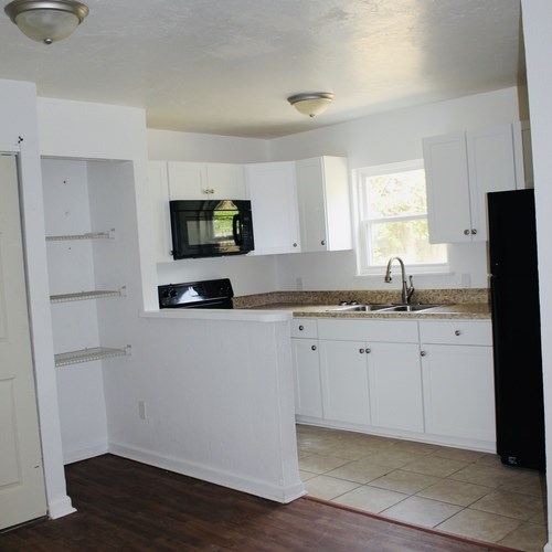 A kitchen with white cabinets and a black refrigerator.