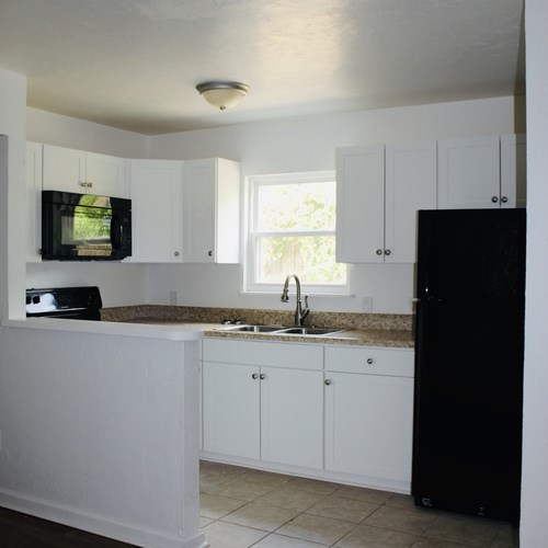 A kitchen with white cabinets and a black refrigerator.