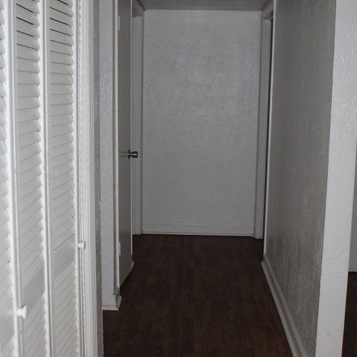 A hallway with a door and a wooden floor.