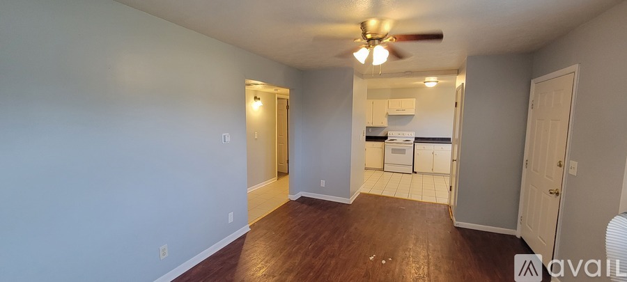 A room with a fan and a kitchen in the background.