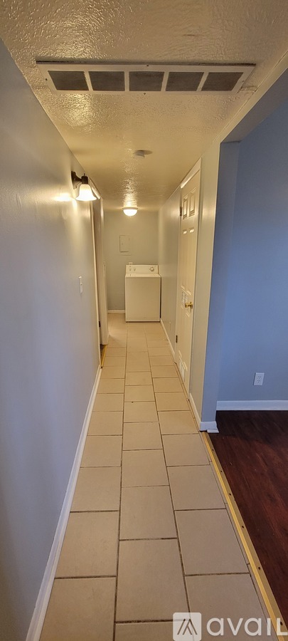 A long hallway with tiled floors and a white refrigerator in the distance.