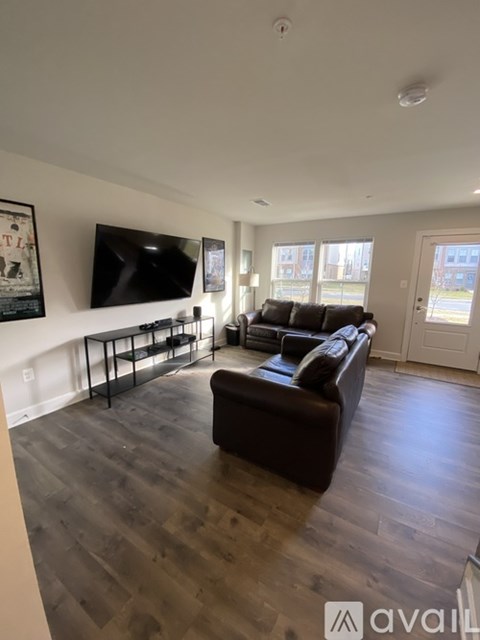 A living room with a brown leather couch and a flat screen TV mounted on the wall.