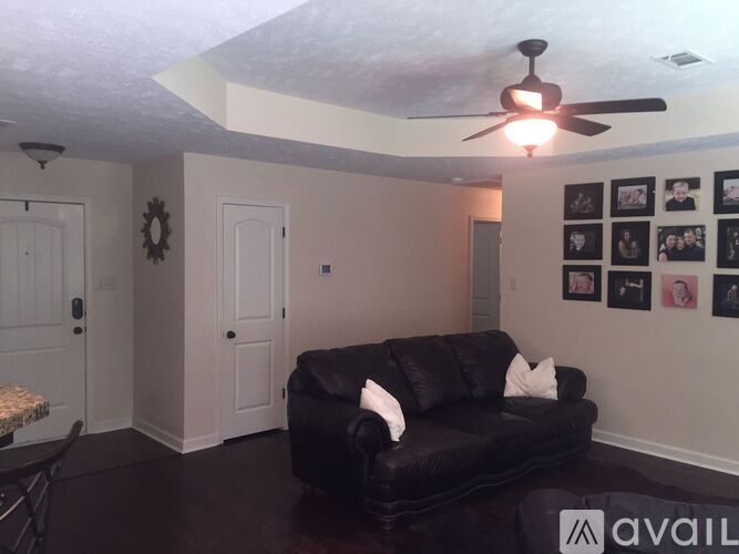 A living room with a black leather couch and a ceiling fan.
