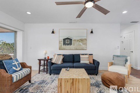 A living room with a blue couch and a painting of a house on the wall.