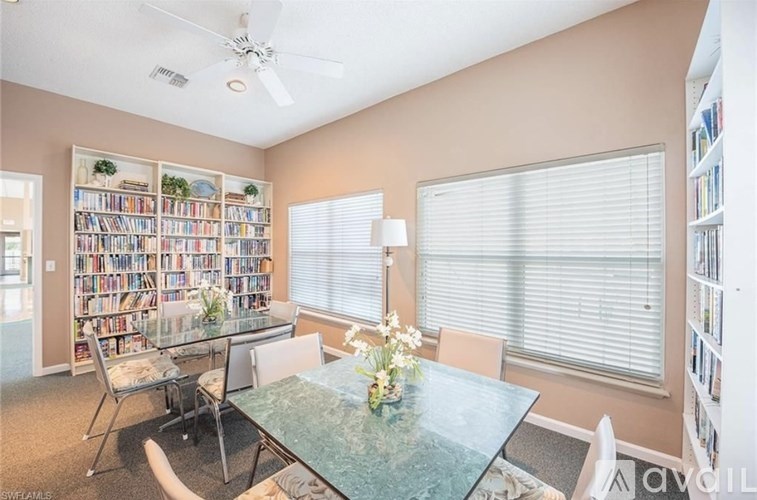 A room with a glass table, chairs, and a bookshelf filled with books.