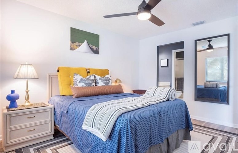 A bedroom with a blue bedspread and a ceiling fan.