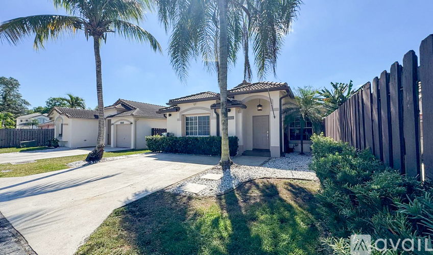 A house with a white fence and palm trees in front.