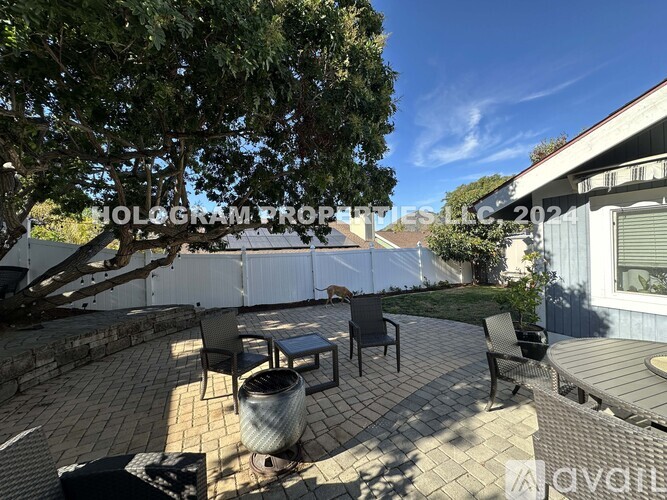 A patio with a table and chairs is surrounded by a white fence and trees.