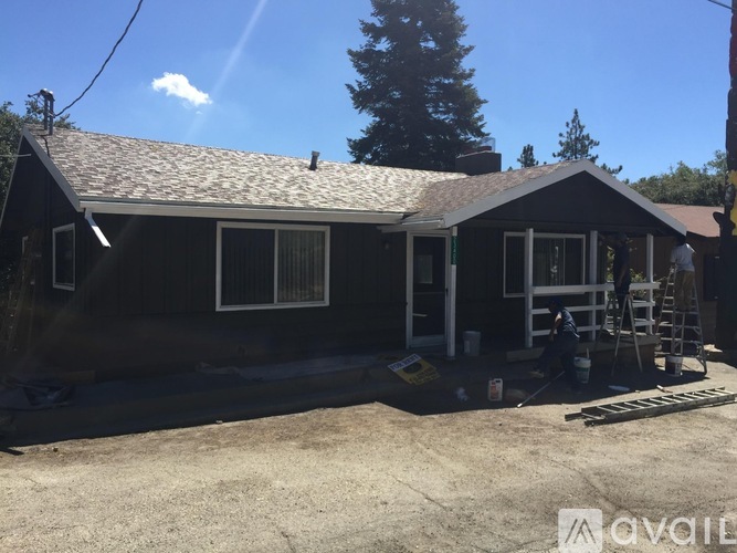 A house with a black roof and white trim is under construction with a ladder and tools on the porch.