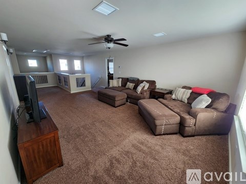 A living room with a brown carpet and a ceiling fan.
