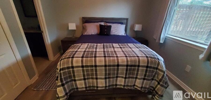 A bed with a plaid comforter and two pillows is in a room with a window.