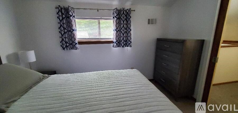 A bedroom with a white bed and a window with curtains.