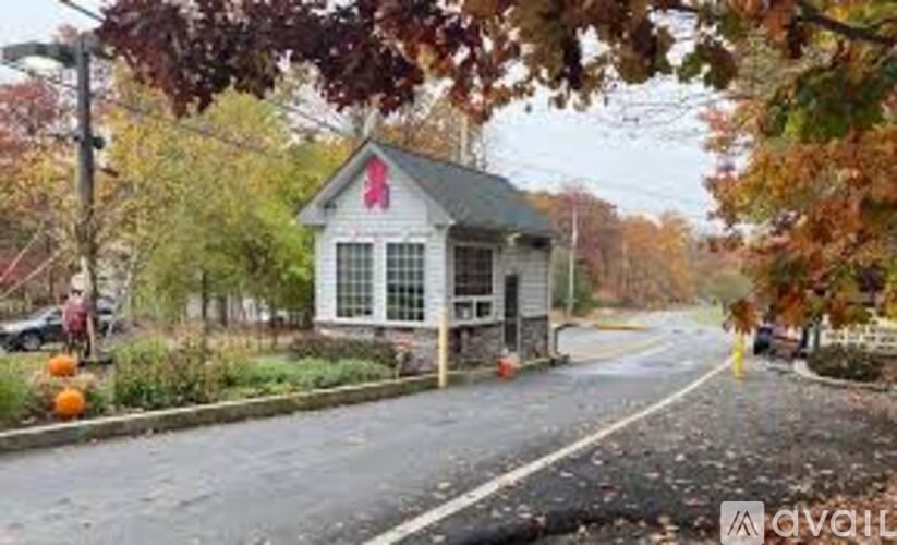 A small house with a red cross on the front is surrounded by trees with autumn leaves.