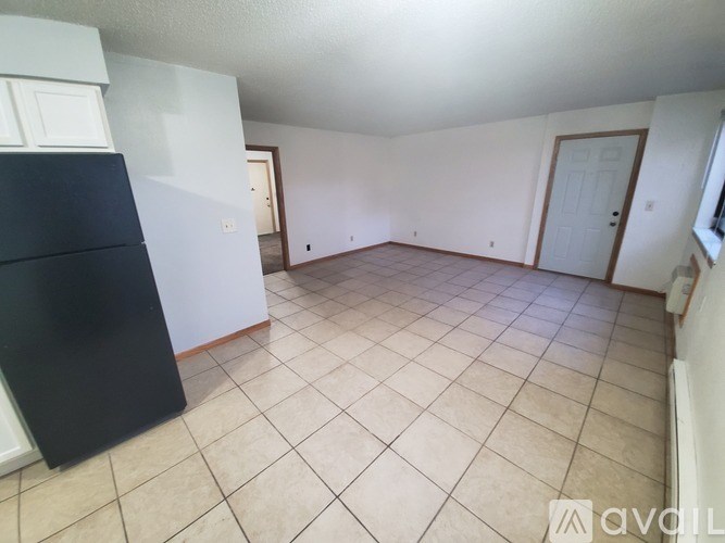 A black refrigerator stands in a room with white walls and tile flooring.