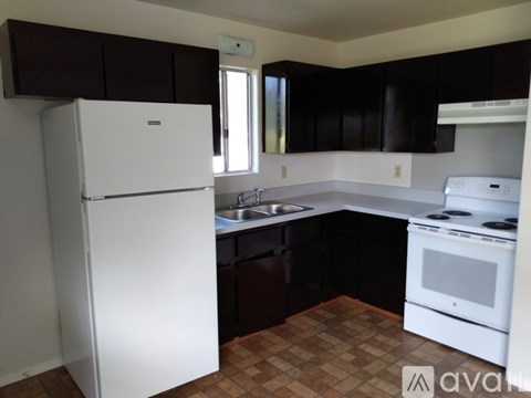 A white refrigerator stands in a kitchen with brown cabinets and a white stove.