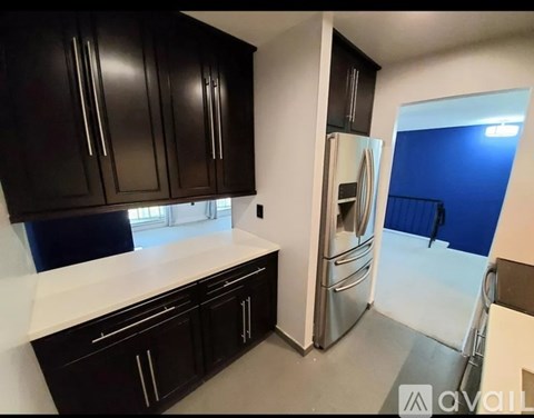 A kitchen with black cabinets and a stainless steel refrigerator.