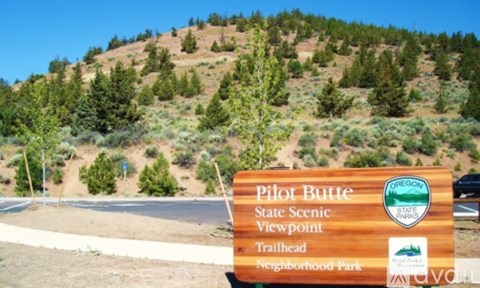 A sign for Pilot Butte State Scenic Viewpoint stands in front of a forested hill.