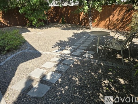 A patio with a table and chairs is surrounded by a gravel path and a wooden fence.