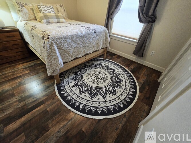 A bedroom with a bed, wooden floor, and a patterned rug.