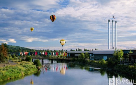A group of hot air balloons flying over a river with a building in the background.
