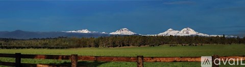 A mountain range with snow capped peaks in the distance behind a green field.