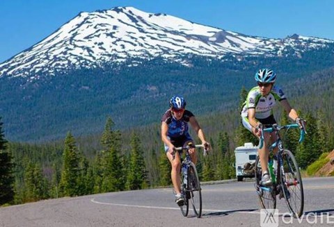 Two cyclists riding on a road with a snow-capped mountain in the background.