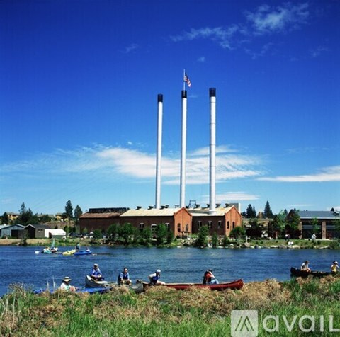 A group of people are kayaking in front of a building with three tall white chimneys.
