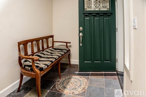 A wooden bench with a cushion sits in front of a green door.