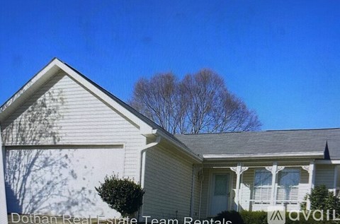 A house with a white siding and a grey roof with a tree in the background.