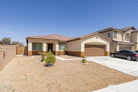 A house with a brown roof and tan walls has a car parked in front.