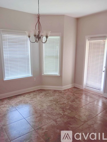 A room with a chandelier, two windows with blinds, and a tiled floor.